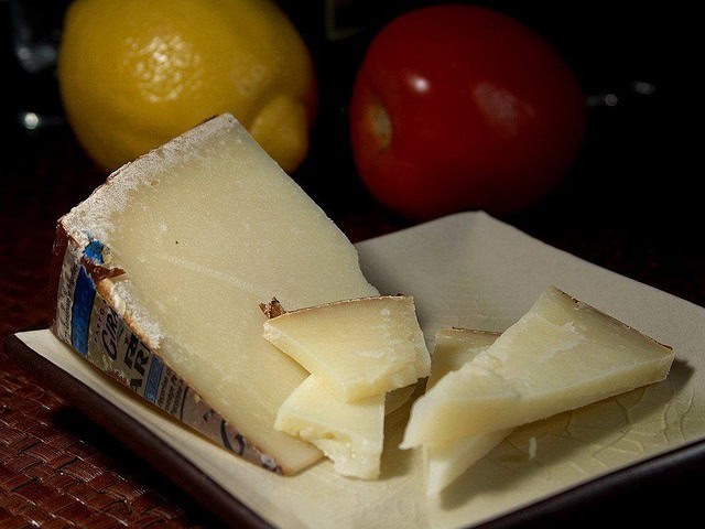 Pecorino sardo cheese — Slices of traditional Sardinian sheep’s cheese displayed with lemons and tomatoes in the background.