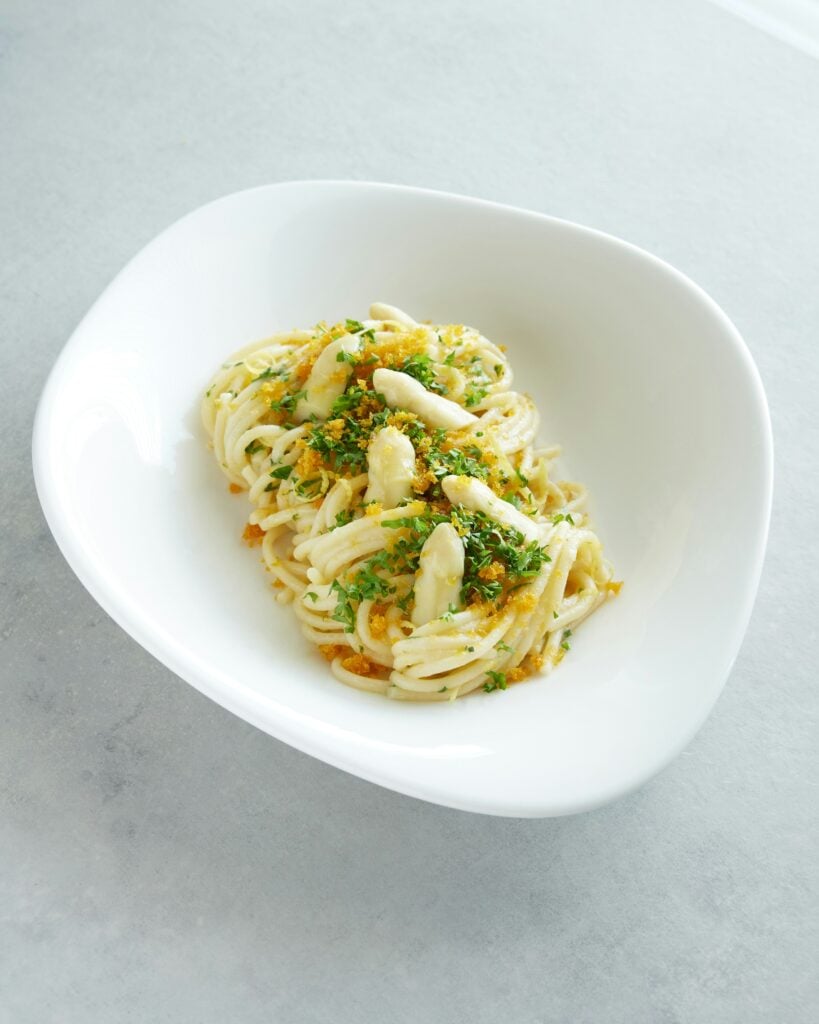 Spaghetti with bottarga — A bowl of spaghetti topped with grated bottarga (cured fish roe), olive oil, and fresh herbs, served in a white dish.