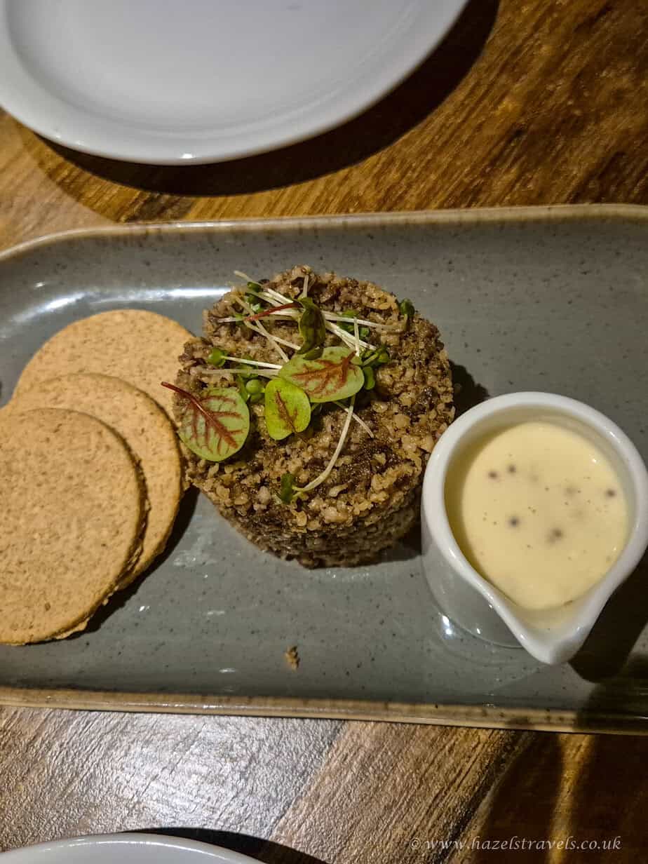 Close-up of Scottish haggis with oatcakes and whisky sauce, garnished with microgreens on a restaurant table.