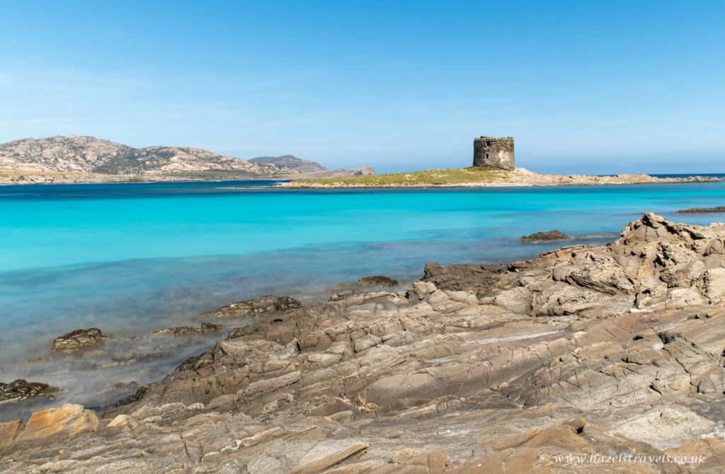 La Pelosa Beach, Sardinia - Brilliant turquoise water and rugged rocks with the historic watchtower in the background.