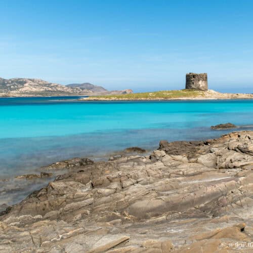 La Pelosa Beach, Sardinia - Brilliant turquoise water and rugged rocks with the historic watchtower in the background.