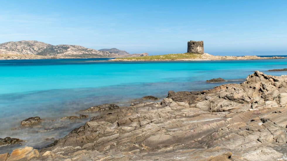 La Pelosa Beach, Sardinia - Brilliant turquoise water and rugged rocks with the historic watchtower in the background.