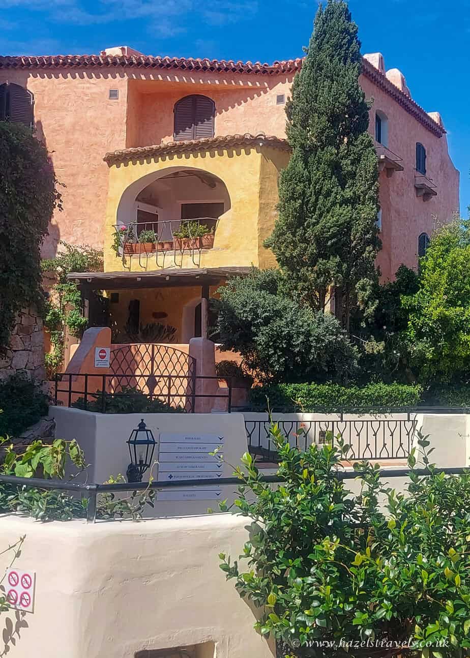 Mediterranean-style villa in Porto Cervo, Sardinia, with peach-coloured walls, arched balconies, and lush greenery under a bright blue sky.