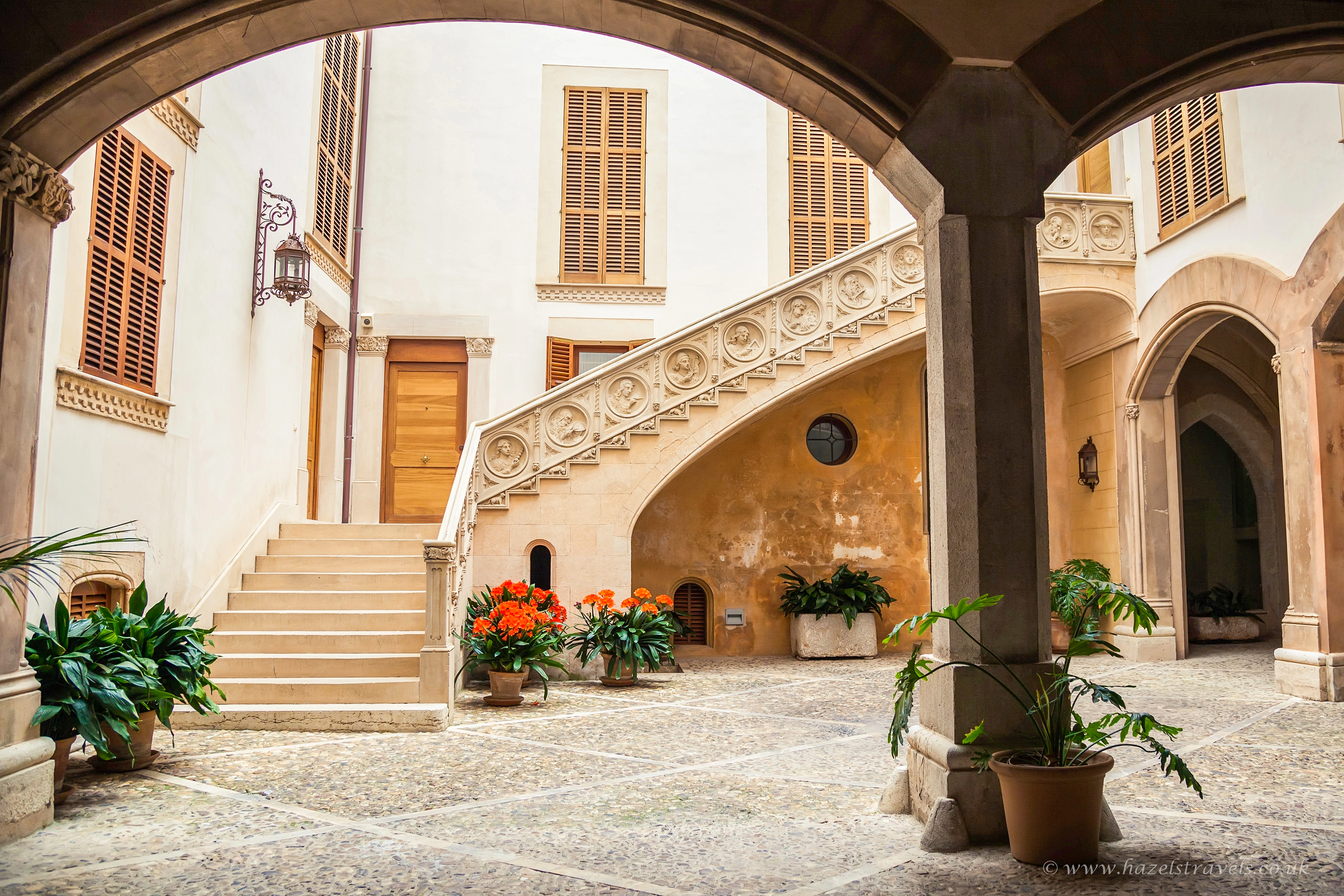 Cozy Palma patio with rustic stone walls, lush potted plants, wooden doors and windows, and dappled sunlight filtering into the courtyard space.