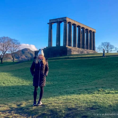 Person walking on Calton Hill, Edinburgh, with the National Monument in the background under a clear blue sky.