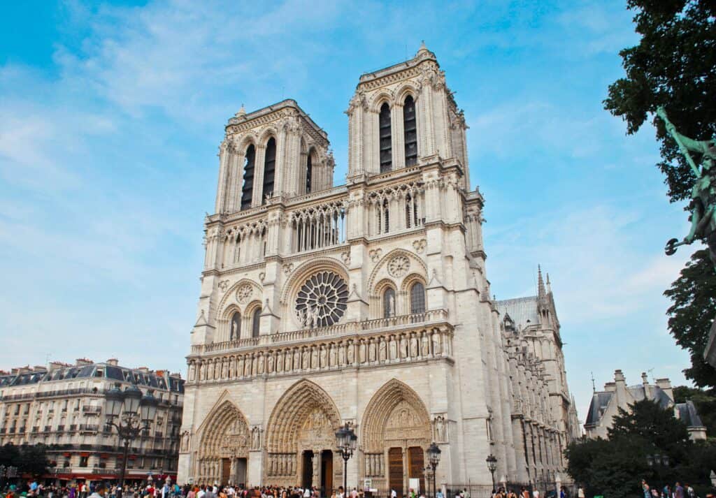 Front view of Notre-Dame Cathedral in Paris, showcasing its twin towers, detailed Gothic architecture, and rose window under a bright blue sky.