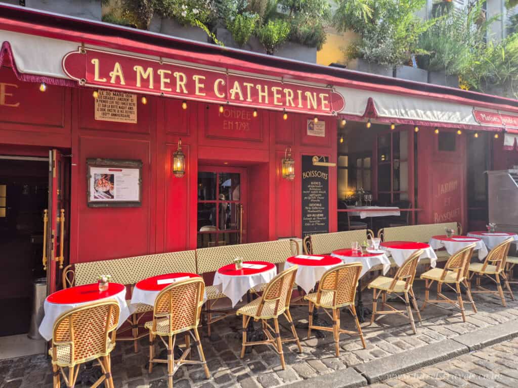 La Mère Catherine café, Montmartre - Classic red Parisian bistro with outdoor seating and vintage signage.