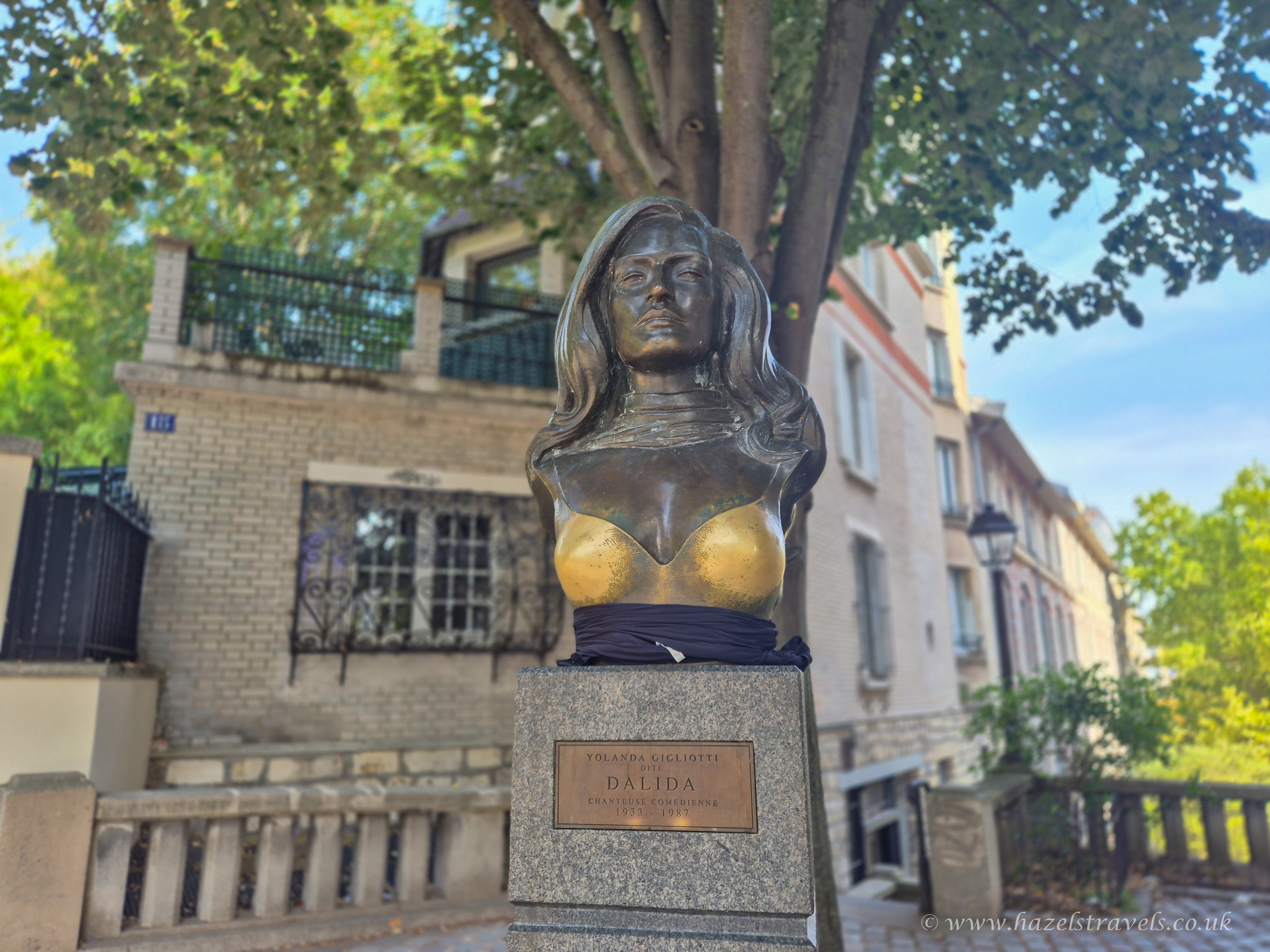 Bronze statue of French-Italian singer Dalida in Montmartre, Paris, surrounded by trees and Parisian buildings.