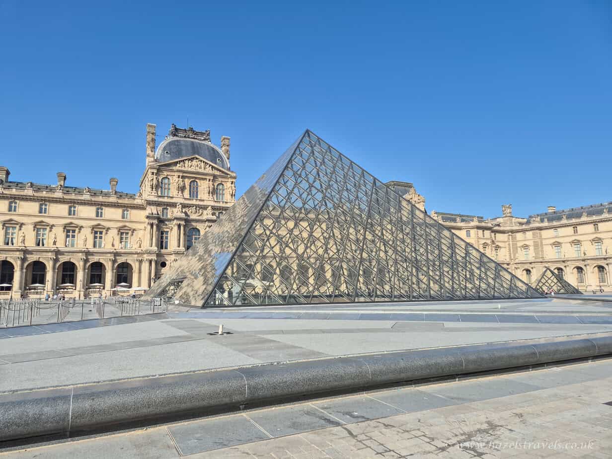 Glass pyramid of the Louvre in Paris against a bright blue sky