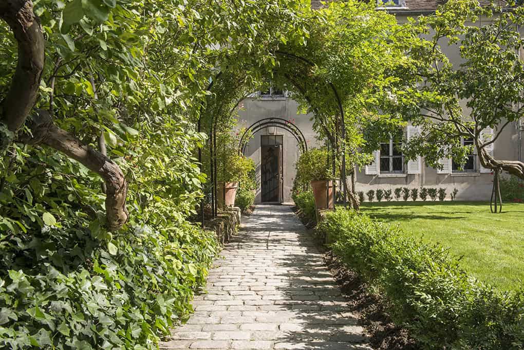 Le Jardin du Musée Montmartre, Paris - Leafy garden pathway leading to the entrance of the Musée Montmartre surrounded by greenery.