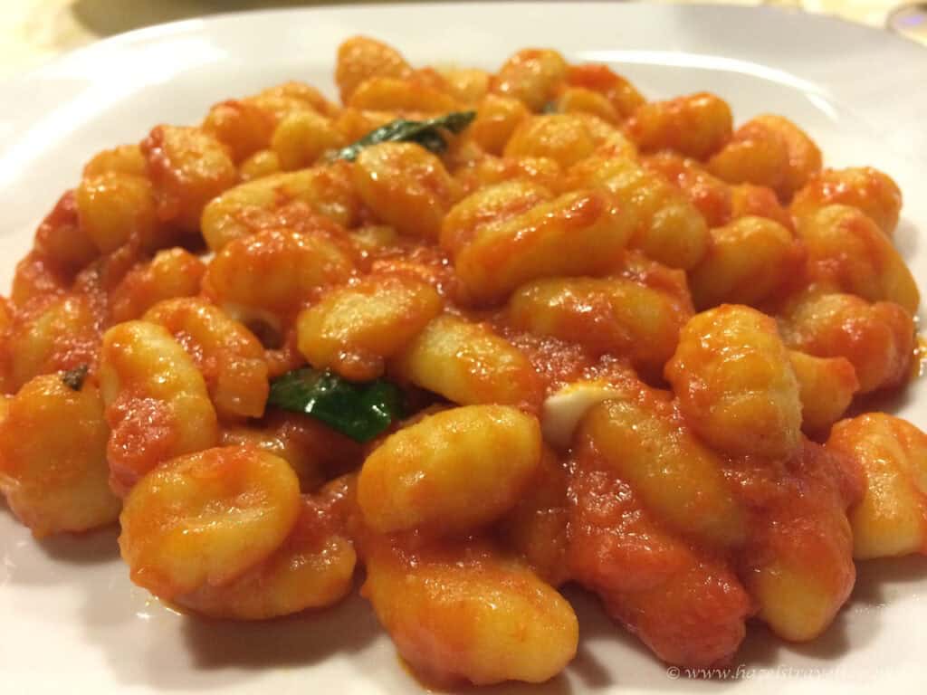 Close-up of Gnocchi alla Sorrentina, soft potato dumplings coated in rich tomato sauce with melted mozzarella and fresh basil, served on a white plate.