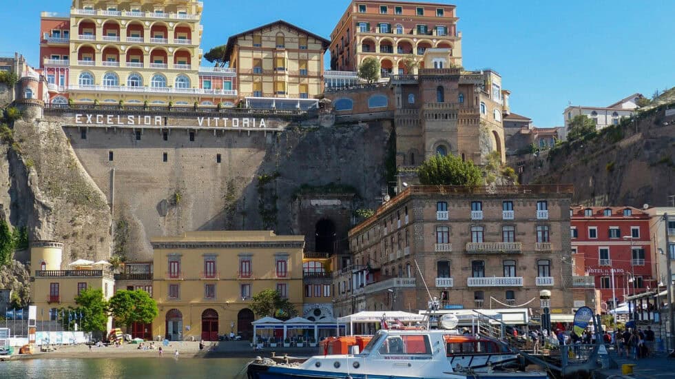 Marina Grande in Sorrento, Italy - colourful waterfront buildings and boats moored in the harbour, with the grand Excelsior Vittoria hotel perched dramatically on the cliff above.