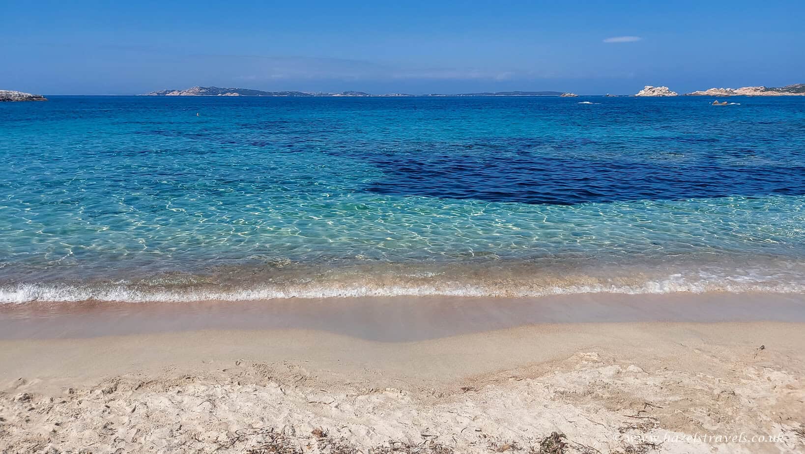 Beach on La Maddalena island, Sardinia — White sand and shallow turquoise sea lapping against rocky shore.