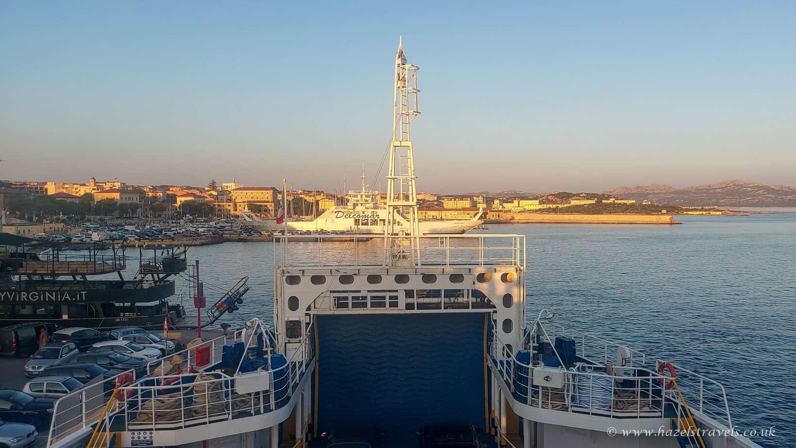 Ferry departing La Maddalena, Sardinia. View from the ferry deck at sunset with port lights and pastel skies.