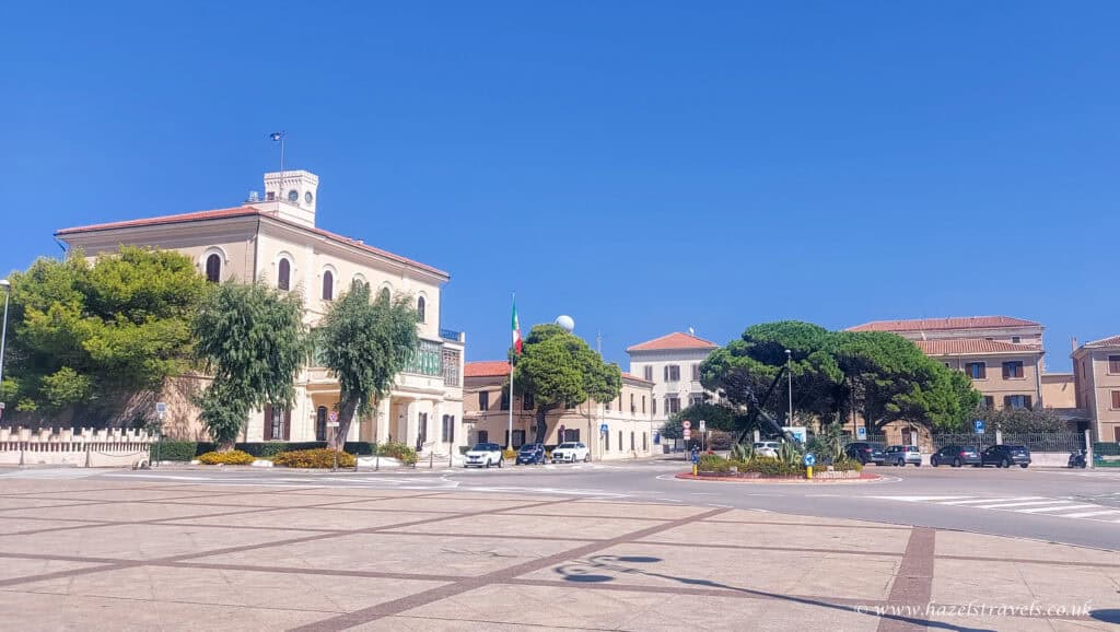 Piazza Garibaldi, La Maddalena - Open square surrounded by pastel buildings and palm trees under a bright blue sky.