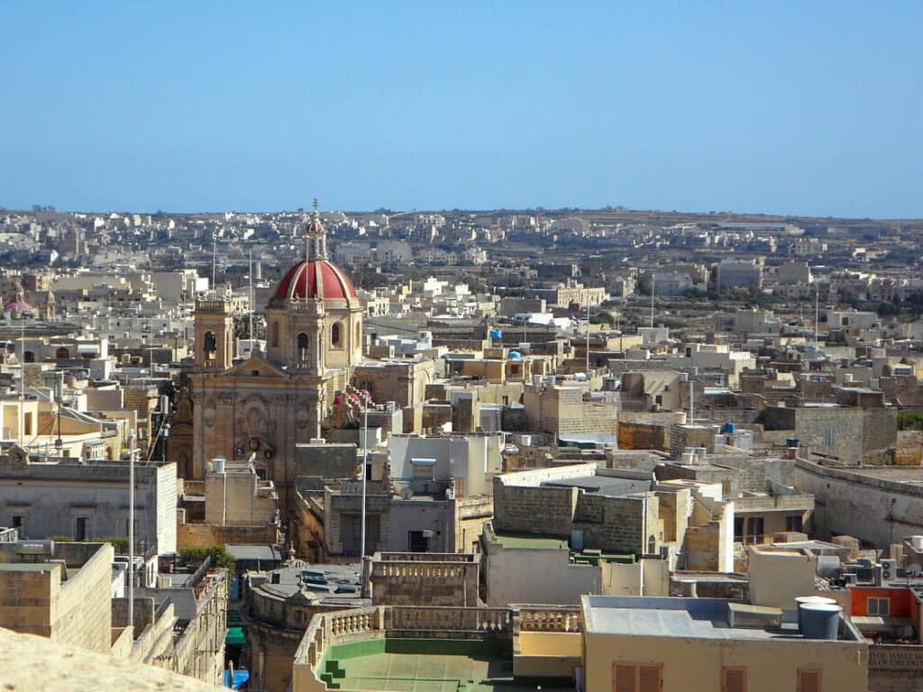 View over Rabat, Malta, showing traditional limestone buildings and the red-domed St Paul’s Church under a clear blue sky.
