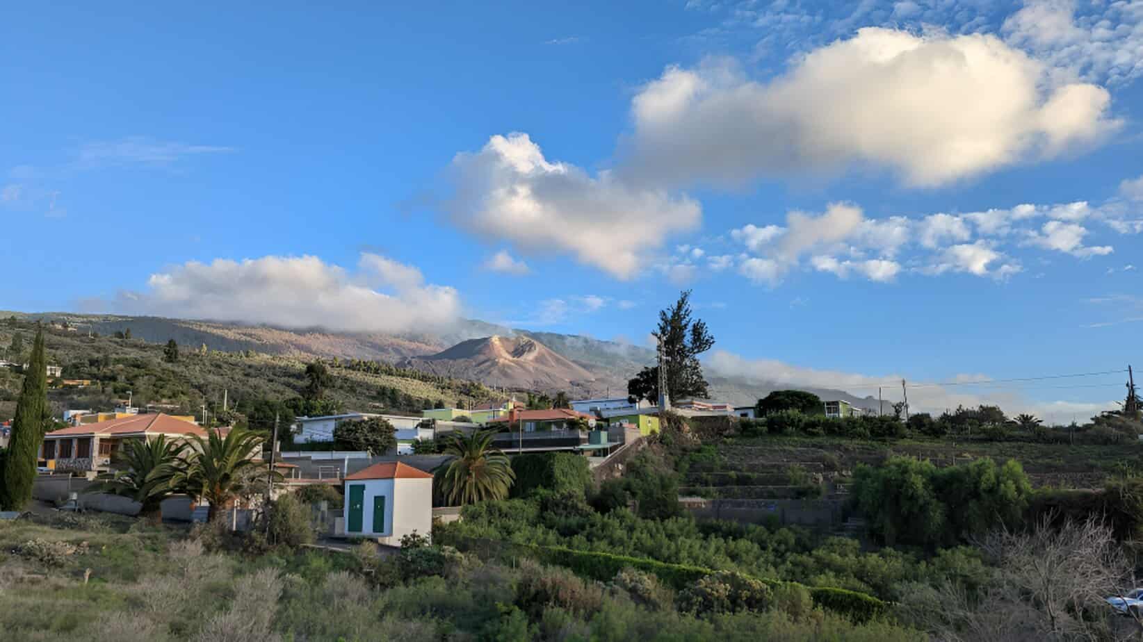 Peaceful rural landscape in La Palma with small houses, a church tower, and the volcano Tajogaite in the background.