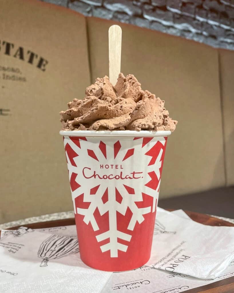Red takeaway cup with a white snowflake design filled with hot chocolate topped with whipped cream and chocolate shavings.