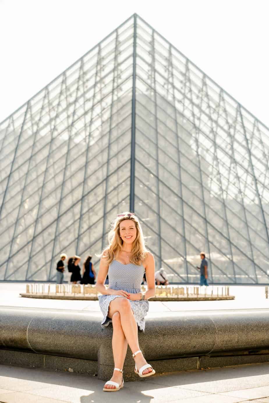 Woman sitting in front of the glass pyramid at the Louvre Museum in Paris on a sunny day
