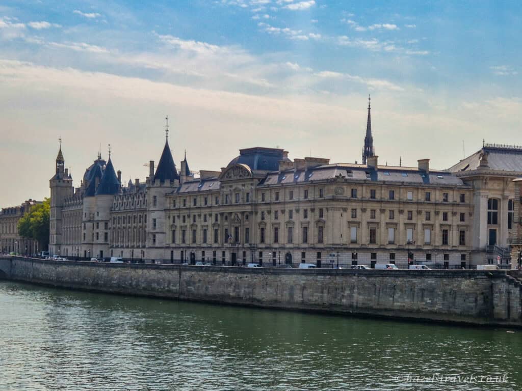 The Conciergerie in Paris, a historic riverside building with pointed towers and Gothic architecture along the River Seine.