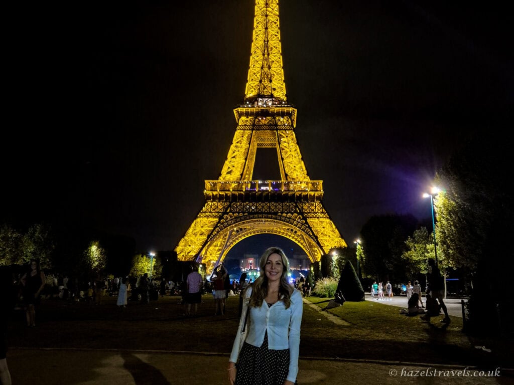 Eiffel Tower at night, Paris — Woman standing in front of the illuminated Eiffel Tower glowing golden against the night sky.