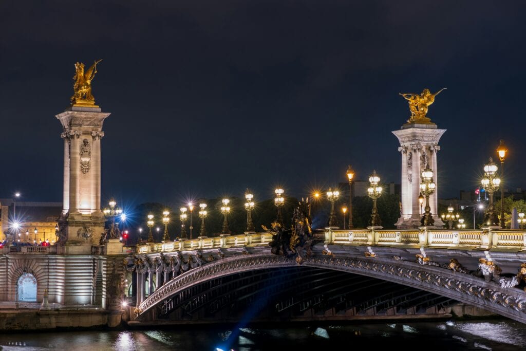 Pont Alexandre III bridge, Paris — Ornate bridge glittering with streetlights reflected in the River Seine at night.