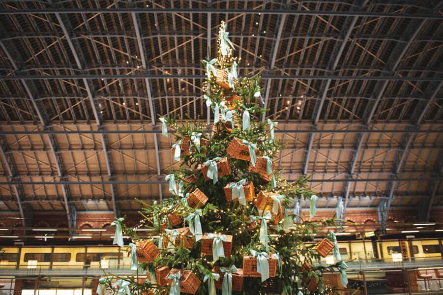 Fortnum & Masonâthemed Christmas tree at St Pancras International, decorated with wicker hampers and pale turquoise ribbons, glowing with warm fairy lights beneath the stationâs steel and glass roof.