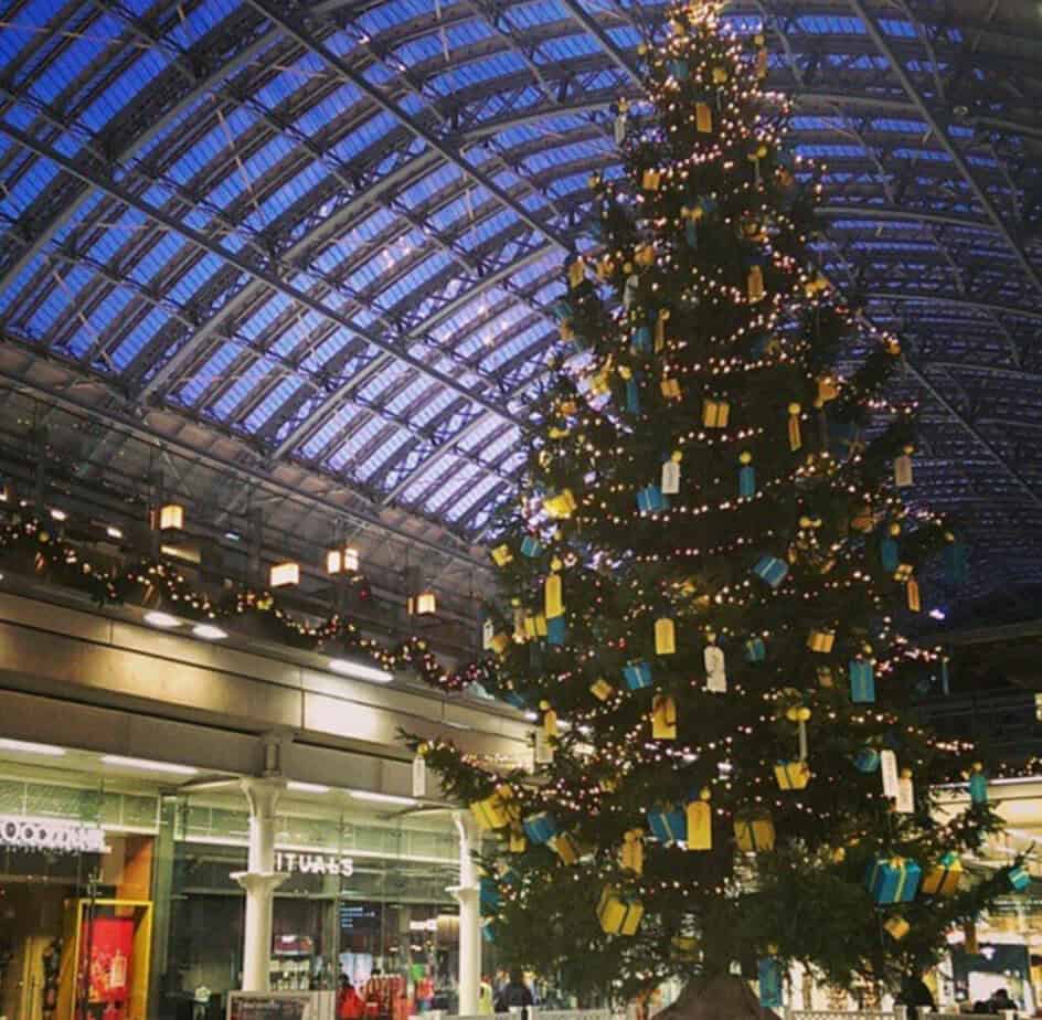 Traditional green Christmas tree covered in gold baubles and warm fairy lights at St Pancras station.