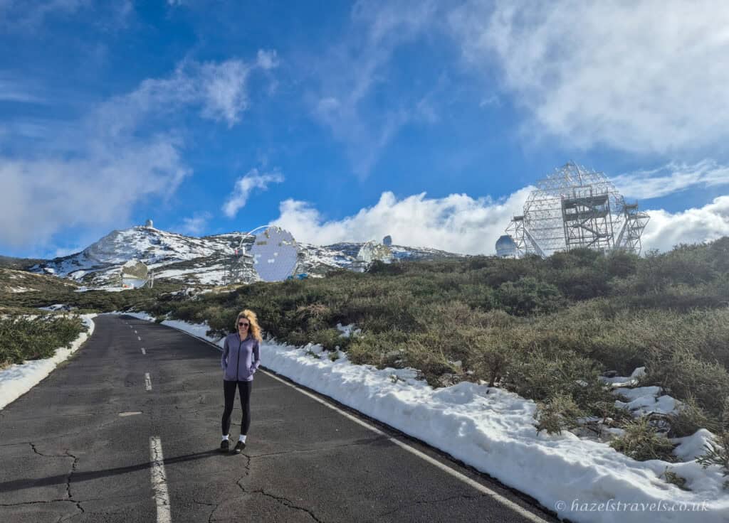 Snow-dusted road on La Palma with person walking beneath a blue sky with Roque de los Muchachos observatory in the background.