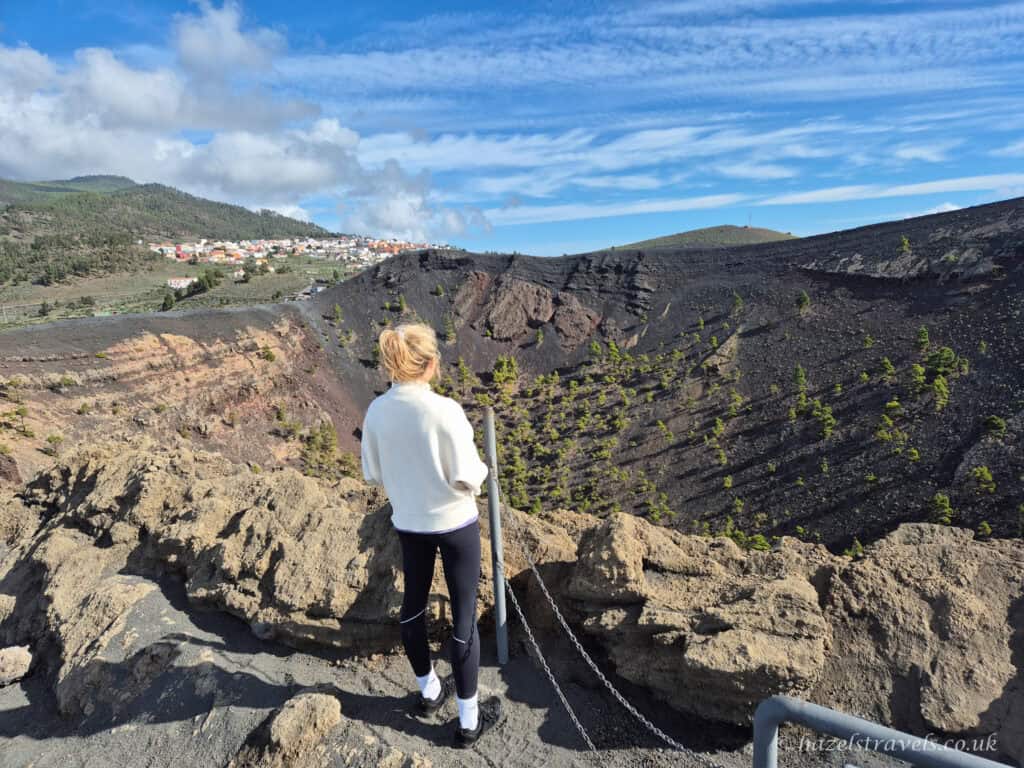 Hiker with blonde hair standing on volcanic rock path overlooking La Palma’s dramatic volcanic terrain at San Antonio Volcano.