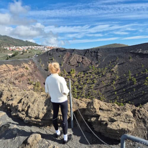 Hiker with blonde hair standing on volcanic rock path overlooking La Palma’s dramatic volcanic terrain at San Antonio Volcano.