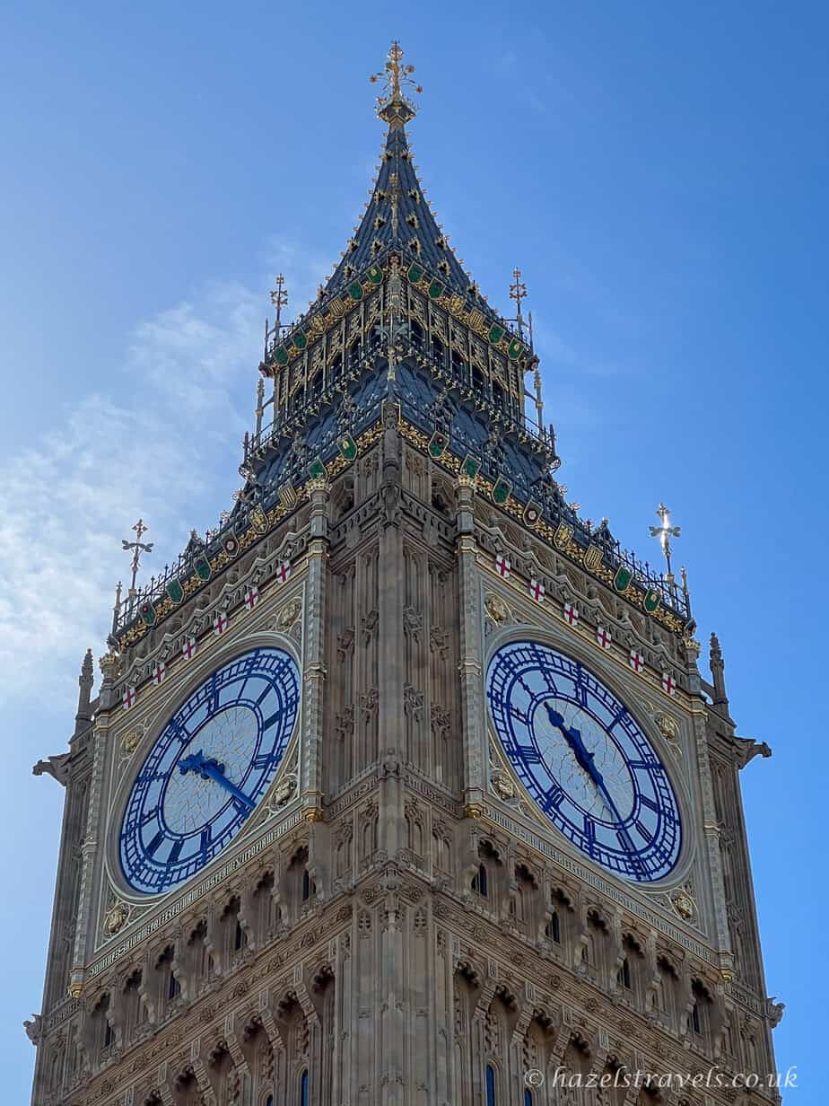 Close-up of Big Ben’s clock tower with gold details shining in the sunlight against a blue sky.