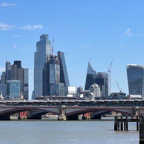 London skyline with modern skyscrapers including the Walkie Talkie and the Cheesegrater, viewed from across the River Thames under a clear blue sky.