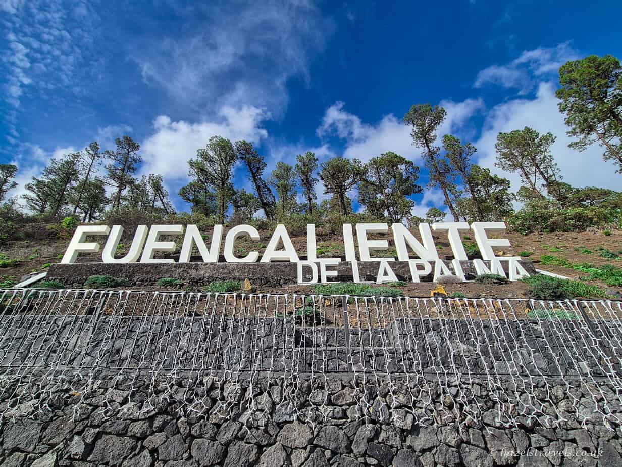 White FUENCALIENTE sign surrounded by palm trees under clear blue skies in southern La Palma.