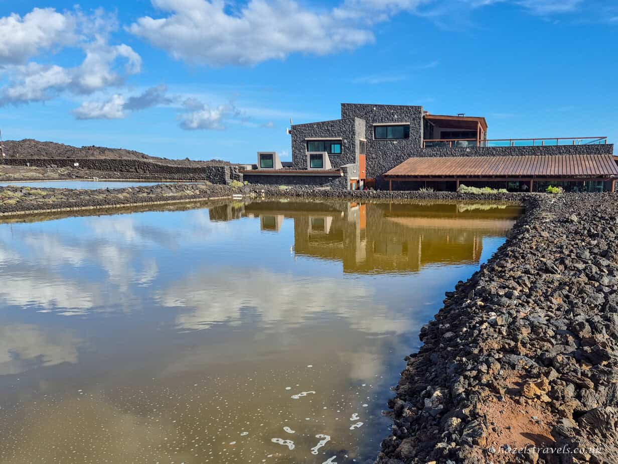 Fuencaliente Salt Flats in southern La Palma, with shallow reflective salt ponds and a modern visitor centre under a blue sky with clouds.