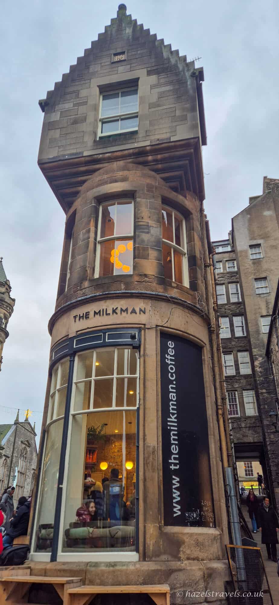 The Milkman café exterior in Edinburgh, a small historic stone building with warm lights glowing inside