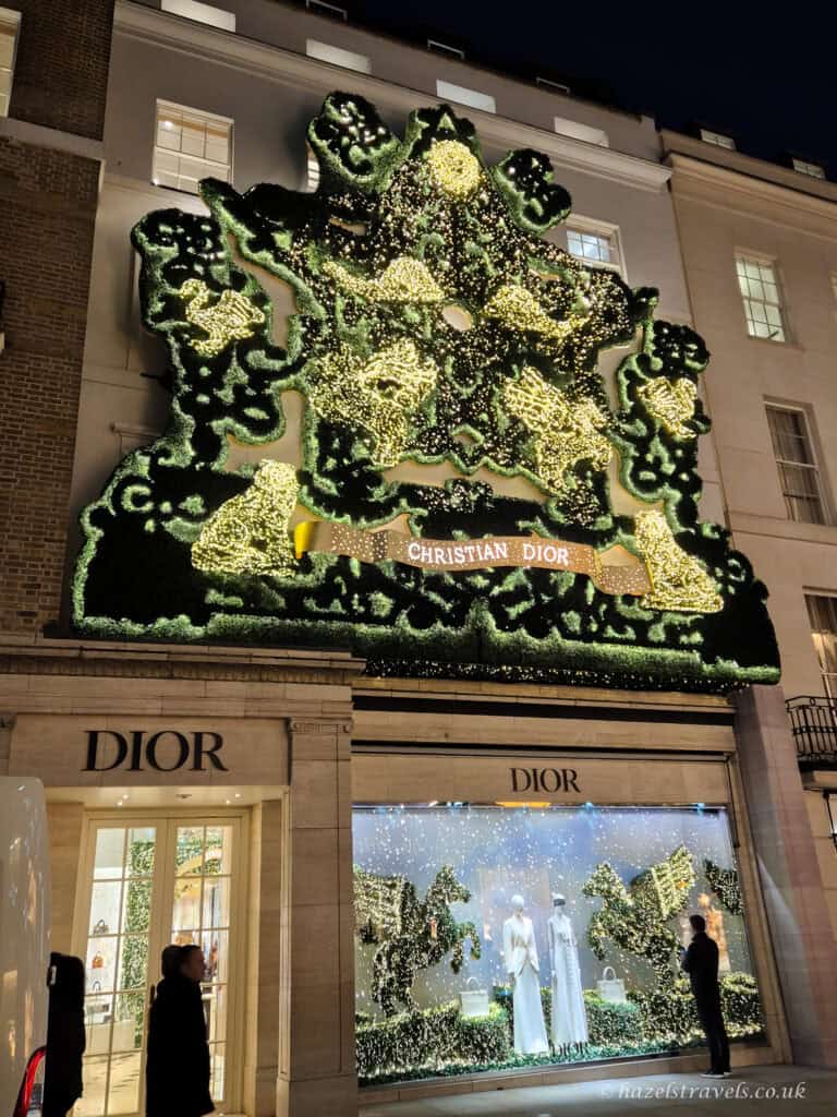 Christian Diorâs London storefront covered in an elaborate green and gold illuminated Christmas display, with glowing floral patterns and festive window decorations beneath the façade.
