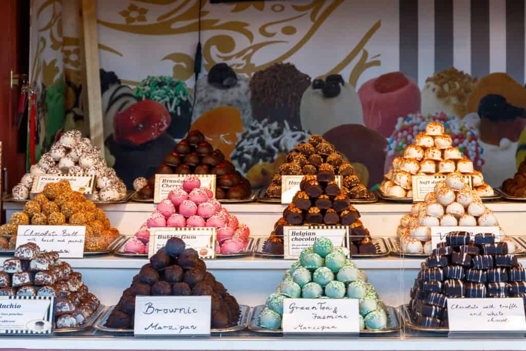 Colourful display of assorted chocolate truffles and marzipan treats at a London Christmas market stall, with handwritten signs and a festive backdrop.