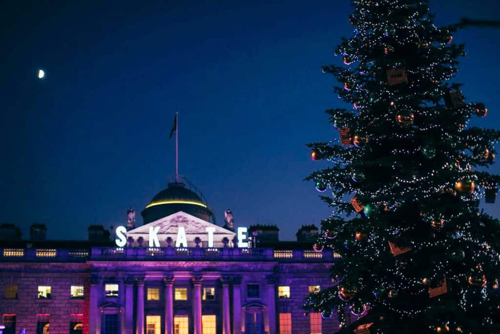Somerset House at night with a large Christmas tree beside the ice rink in London