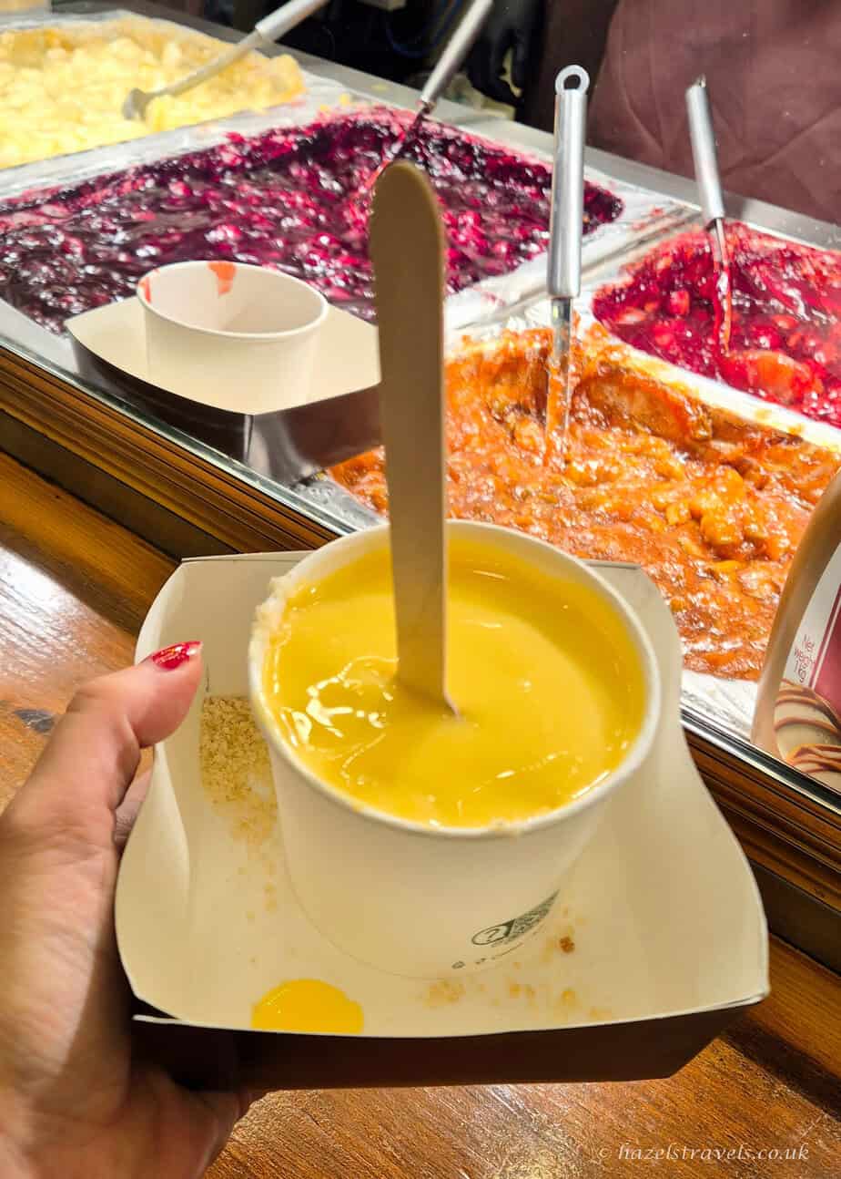 Apple crumble dessert from the Edinburgh Christmas Market, served warm in a paper bag with custard and a wooden spoon"