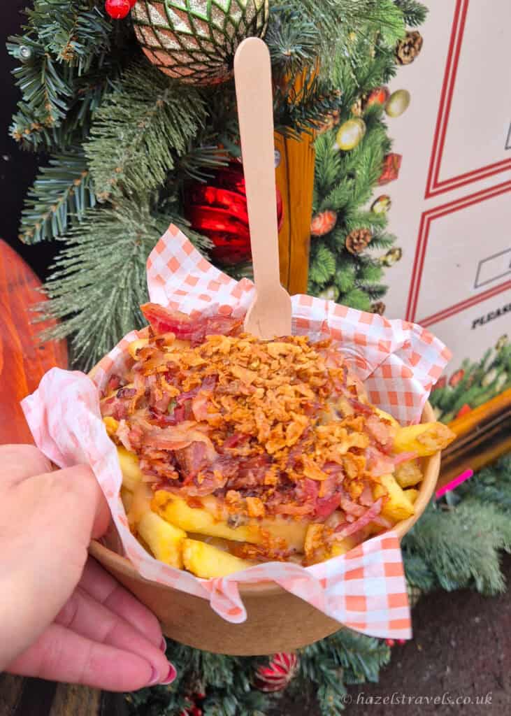 Festive fries topped with haggis, peppercorn sauce and crispy onions at the Edinburgh Christmas Market, served in a cardboard bowl with a wooden fork