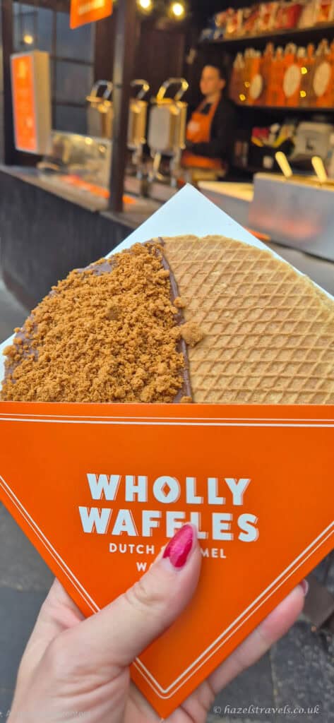 Biscoff stroopwaffel from Wholly Waffles at the Edinburgh Christmas Market, served in an orange paper cone with crumb topping and waffle visible