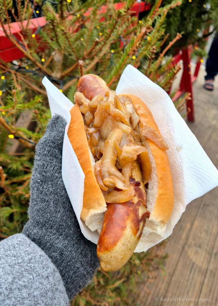 Bratwurst in a crusty bread roll topped with fried onions at the Edinburgh Christmas Market, held in a gloved hand