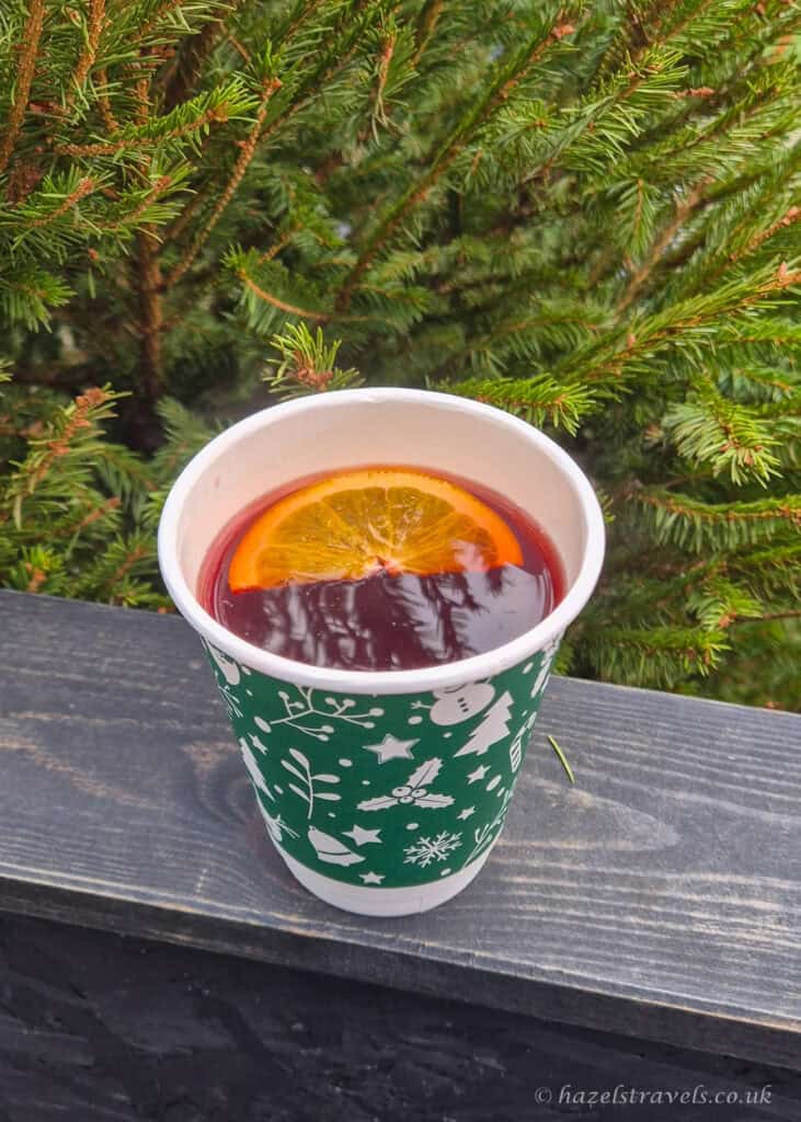 Cup of mulled wine with an orange slice in a festive paper cup at the Edinburgh Christmas Market, set against evergreen trees