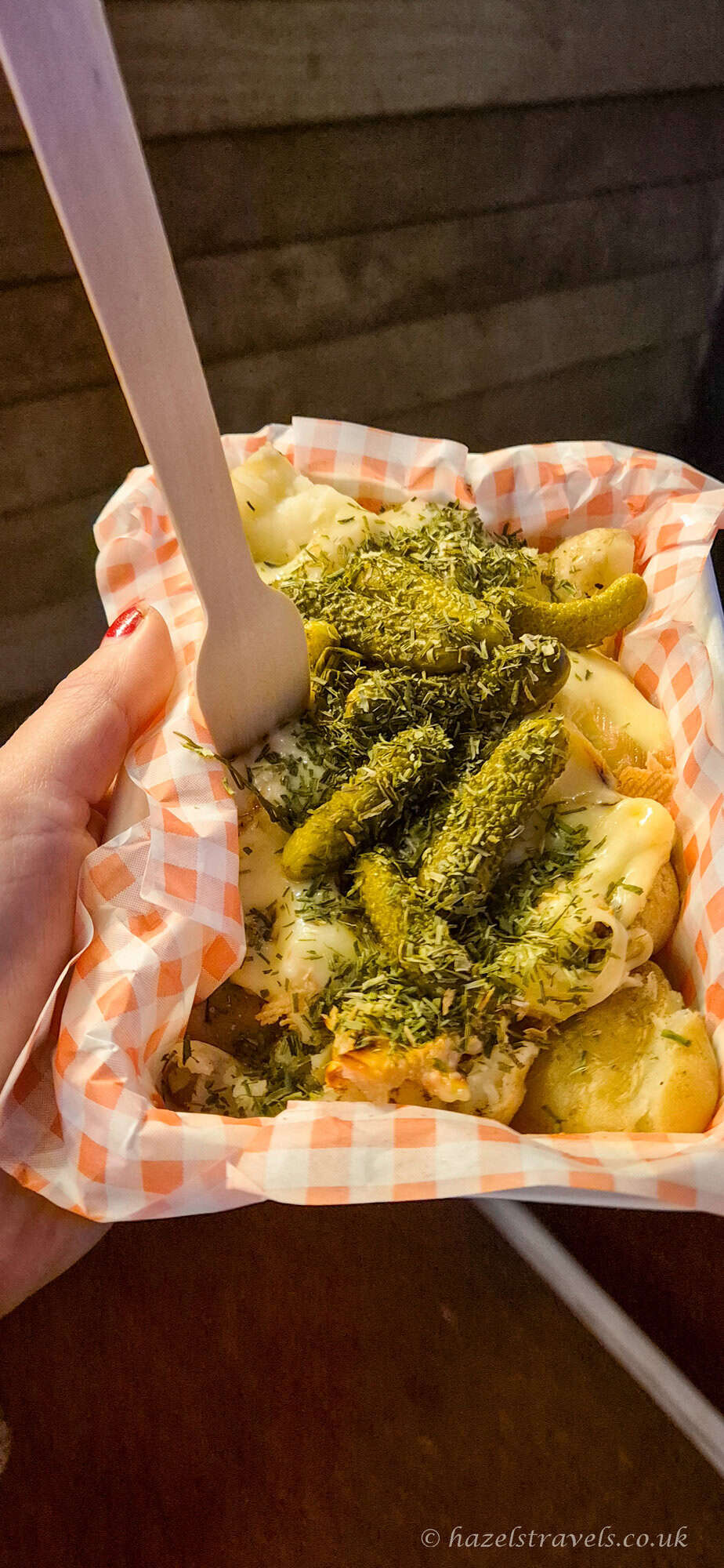 Raclette cheese scraped over potatoes with cornichons at the Edinburgh Christmas Market, served in a paper-lined tray with a wooden fork
