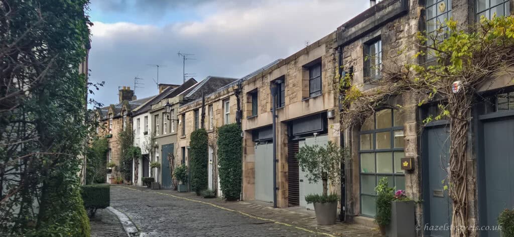 Quiet cobbled street in Edinburgh’s Old Town lined with historic stone houses and greenery on a calm winter day