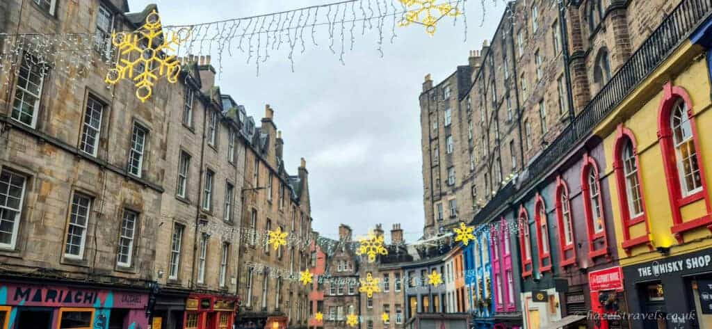 Victoria Street in Edinburgh decorated with hanging snowflake Christmas lights, colourful shopfronts and historic stone buildings