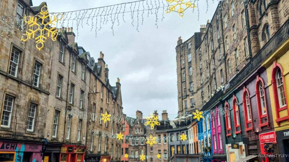 Victoria Street in Edinburgh decorated with hanging snowflake Christmas lights, colourful shopfronts and historic stone buildings