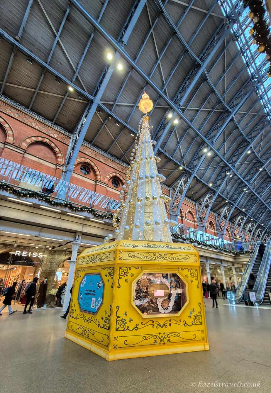 Inside St Pancras International station with the 2025 Christmas tree installation glowing under the glass roof.