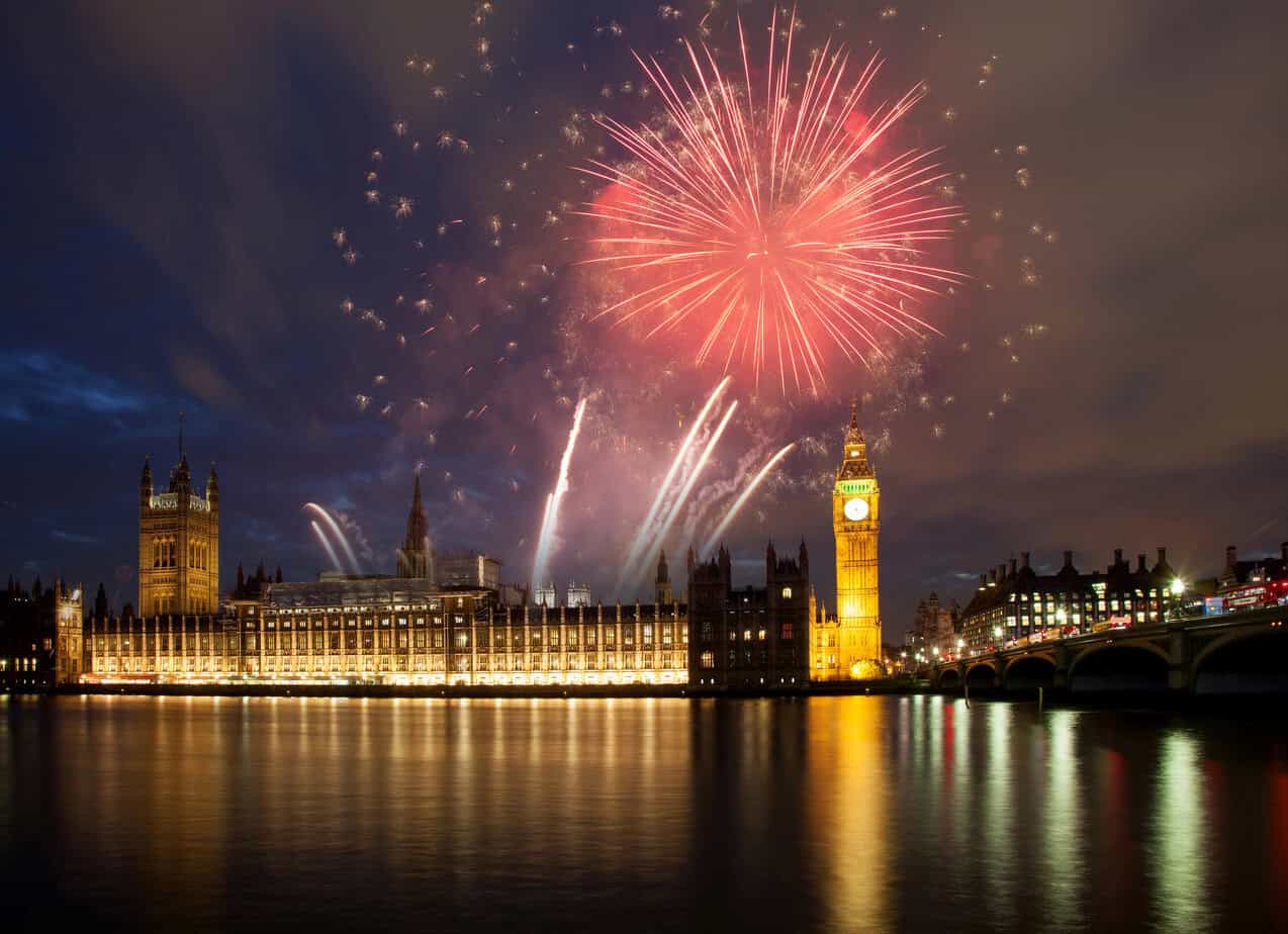 Red and white fireworks bursting over the Houses of Parliament and Big Ben in London on New Year’s Eve, reflected in the River Thames